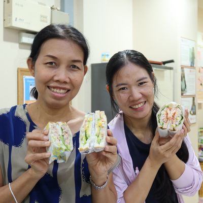 Thip and Fon are smiling while holding a sandwich for the camera at the Better Me Connect Workshop.